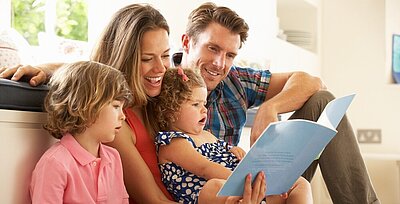 A mother, father, brother and sister sitting reading a book.